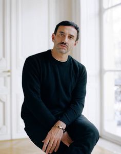 a man sitting on top of a wooden floor in front of a white wall and window