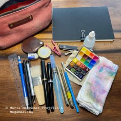 the contents of a travel bag laid out on top of a wooden table next to a notebook