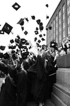 black and white photograph of graduates throwing their caps in the air at graduation ceremony on campus