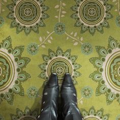 a pair of black shoes standing in front of a green and white floral wallpaper