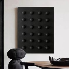 a dining room table with a black plate on top of it next to a wall mounted art piece