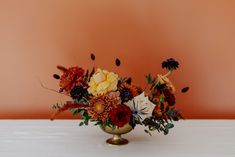 a vase filled with lots of flowers on top of a white table next to an orange wall