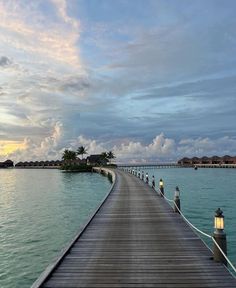 a long dock leading into the ocean with lights on each end and palm trees in the distance