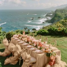 an outdoor table set up with flowers and plates on it, overlooking the water's edge