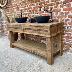 an old wooden table with two black bowls on it and a brick wall in the background