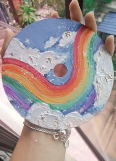 a person holding up a painted disc with a rainbow on it's side in front of a window