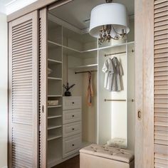 an open closet with clothes hanging on the door and a bench in front of it