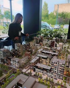 a woman standing in front of a model of a city with lots of tall buildings