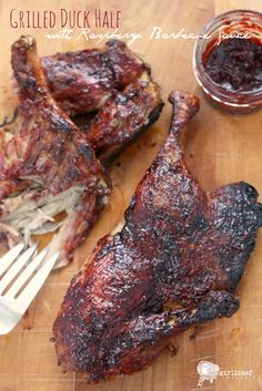 grilled duck half on a cutting board next to a fork and bbq sauce