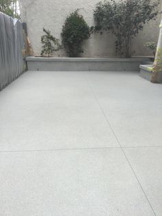 an empty concrete patio in front of a wall with plants growing on the side and behind it