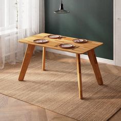 a wooden table with plates on it in front of a green wall and white curtains