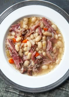 a white bowl filled with meat and beans on top of a blue cloth covered table