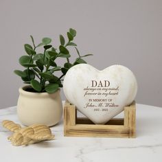 a heart shaped vase with a plant in it next to a small wooden stand that says dad