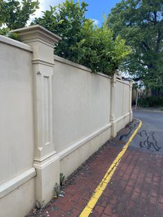 a white fence with green plants on top and yellow line down the middle, next to a brick sidewalk