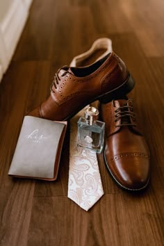 a pair of brown shoes sitting on top of a wooden floor next to a tie