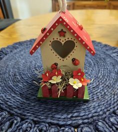 a small birdhouse with flowers and hearts on it's roof sitting on a blue rug