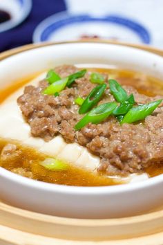 a white bowl filled with meat and vegetables on top of a wooden plate next to chopsticks