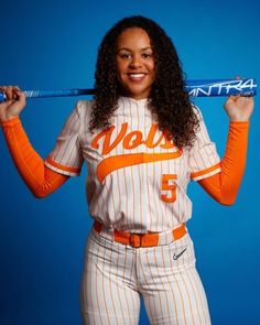 a woman in an orange and white baseball uniform is holding a bat over her head