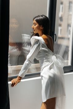 a woman standing in front of a window wearing a white dress