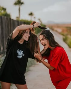 two young women standing next to each other near a fence and palm trees in the background