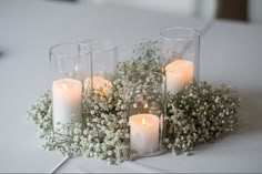 candles are lit in glass vases with baby's breath flowers on the table