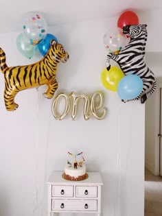 two balloons that say one and a tiger balloon with the word one on it in front of a cake