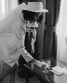 a woman in a white suit and hat leaning over a table