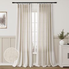 a white curtain hanging on the side of a window next to a wooden cabinet and potted plant