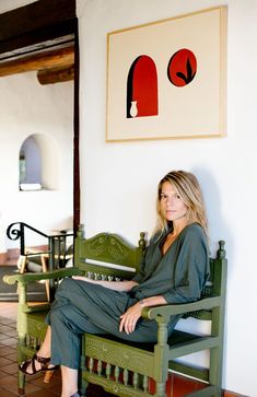 a woman sitting on a green bench in front of a wall with art hanging above it