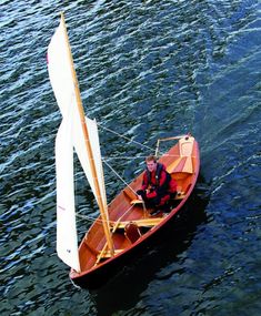 a man is sitting in a small sailboat on the water with no one around