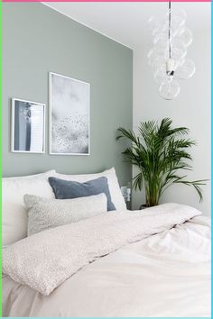 a white bed sitting under a chandelier next to a green potted plant