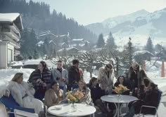 a group of people sitting around a table with drinks in front of snow covered mountains