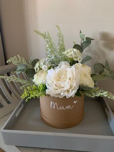 a flower pot with flowers and greenery in it on a tray next to a chair