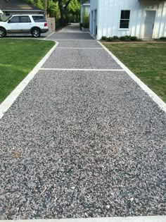 a white car parked on the side of a road next to a driveway with gravel and grass