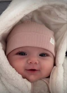 a smiling baby wearing a pink hat and white blanket on top of it's head