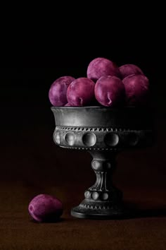 a metal bowl filled with purple fruit on top of a table