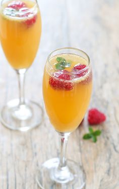 two glasses filled with raspberry lemonade on top of a wooden table next to fresh raspberries