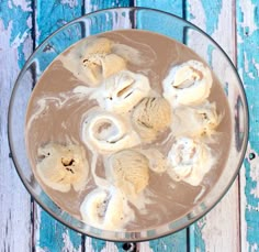 a glass bowl filled with ice cream on top of a blue wooden table next to a spoon