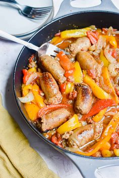 a skillet filled with sausage and peppers on top of a white table cloth next to silverware