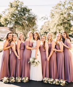 a group of women standing next to each other in long purple dresses and holding bouquets