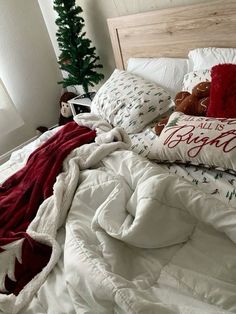 an unmade bed with pillows and blankets on it, next to a christmas tree