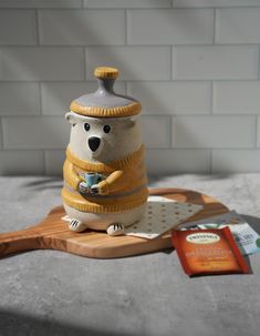 a ceramic bear figurine sitting on top of a cutting board next to a packet of orange juice