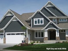 a large gray house with white trim on the front and side windows, two car garage doors