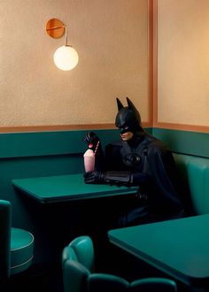 a batman sitting at a table with a drink