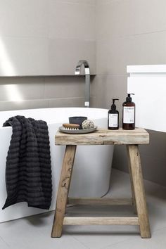 a white bath tub sitting next to a wooden stand with bottles on top of it