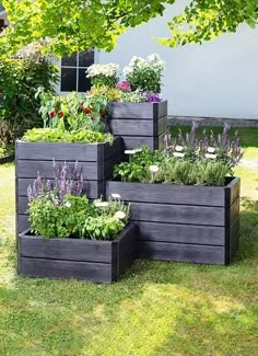 four wooden planters with different types of flowers in them on the grass near a house