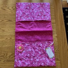 a piece of pink fabric on top of a wooden floor next to a vase with flowers