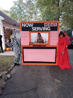 two people dressed up in costumes standing next to a sign that reads now serving information