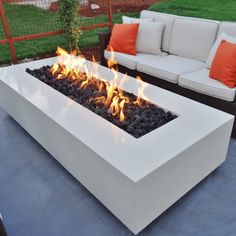 a fire pit sitting on top of a patio next to a white couch and orange pillows