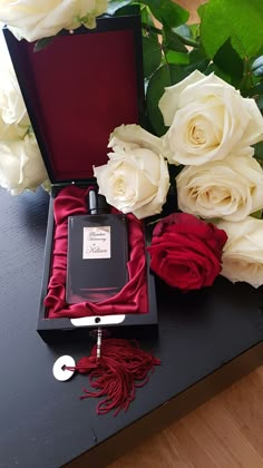 a black box with white roses and a red tassel in it sitting on a table